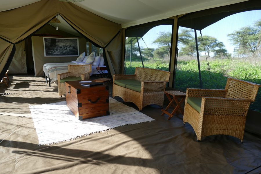 Living-room tent with cane armchairs, a wooden chest and rugs, open to the trees