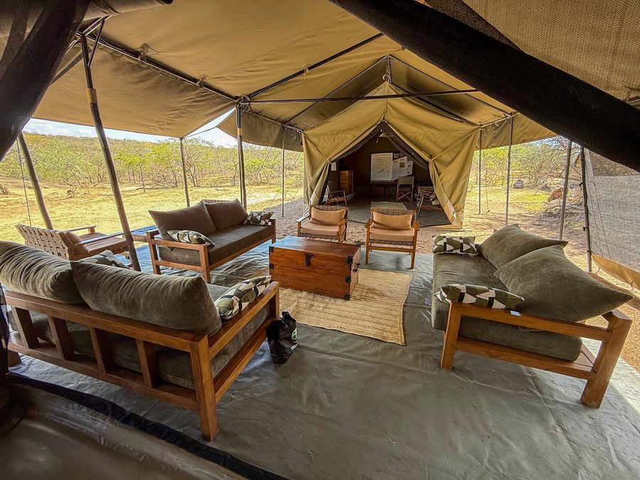Open-sided lounge tent with cushioned sofas and wooden tables looking out over the plains